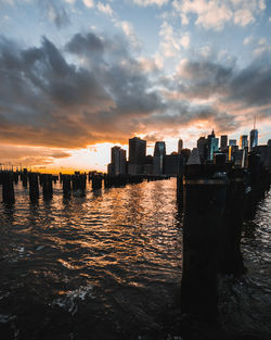 Sea by modern buildings against sky during sunset