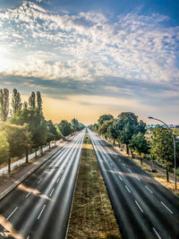 Empty road along plants and trees against sky