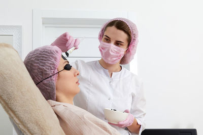 Cosmetologist applying black mask on the face of a beautiful woman for carbon peeling