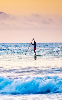 Rear view of man skiing on sea against sky during sunset