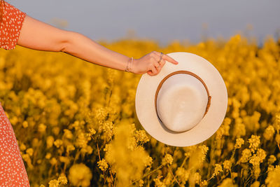 Woman's hand holding a hat close-up in a yellow mustard field