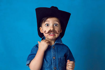 Funny cowboy boy with a mustache and a hat stands in the studio on a blue background