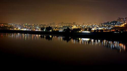 Illuminated buildings by lake against sky in city at night