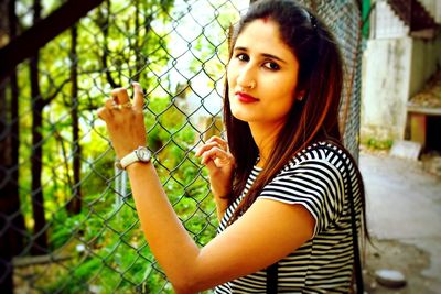 Portrait of young woman standing by fence in park