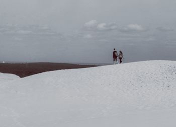 Friends walking on sand dune against sky at desert