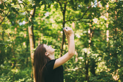 Side view of woman taking selfie in forest