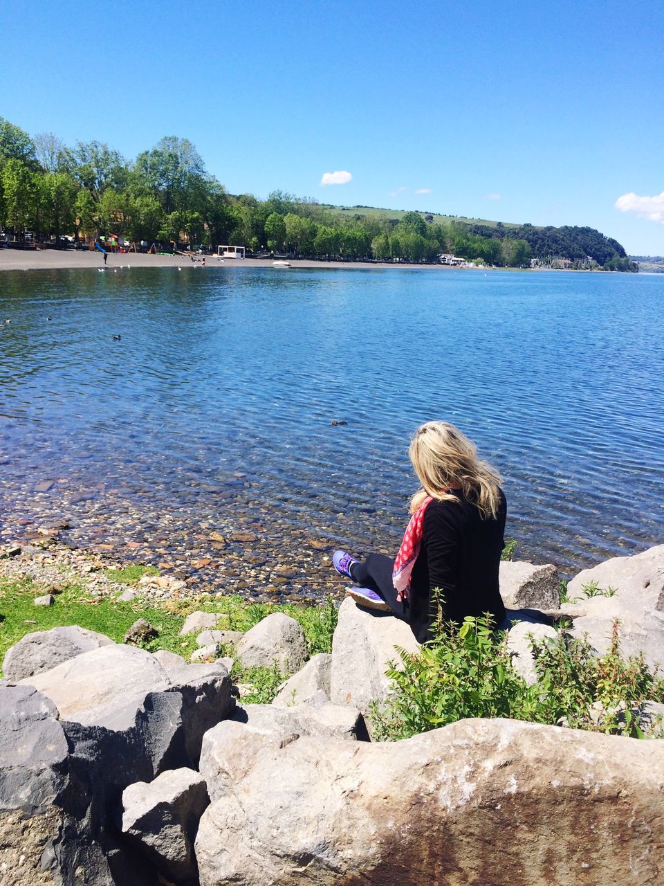 WOMAN SITTING ON ROCK BY LAKE AGAINST SKY