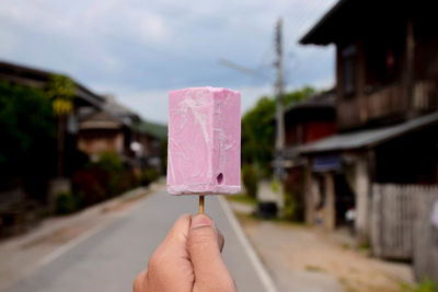 Close-up of hand holding ice cream cone against buildings