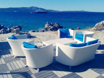 Chairs and table arranged at beach against clear blue sky