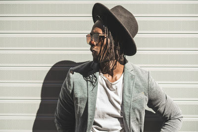 Young man wearing hat while standing against wall in city