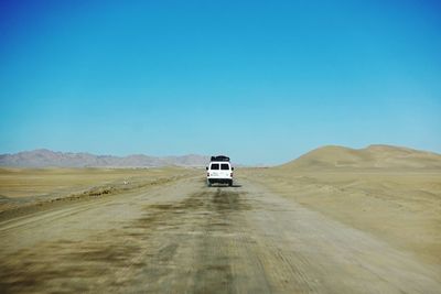 Car on desert land against clear blue sky