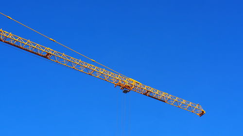 Low angle view of crane against clear blue sky