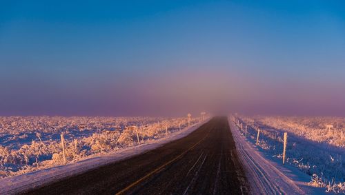 Road amidst landscape against clear sky during winter