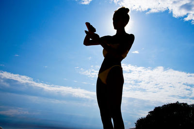 Low angle view of silhouette woman standing against blue sky