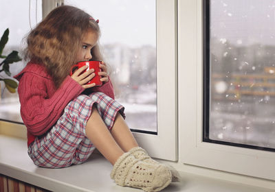 Cute girl drinking hot chocolate sitting by window