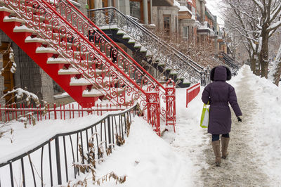 Rear view of woman walking outside buildings on sidewalk during winter