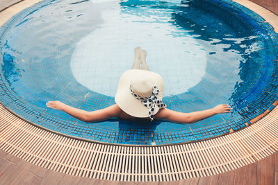 Rear view of mid adult woman wearing hat swimming in pool