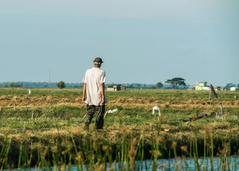 Rear view of man standing on field against clear sky