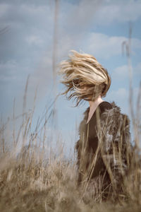 Woman with tousled hair standing on field against sky