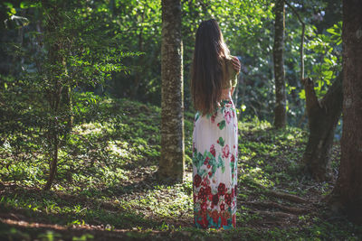 Woman standing by tree trunk in forest