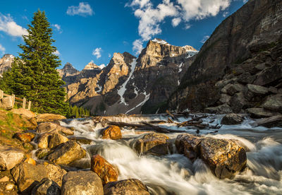 Scenic view of waterfall by mountains against sky