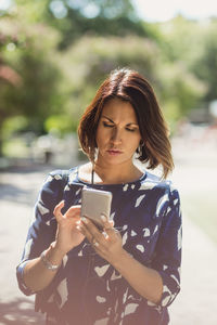 Mature businesswoman using smart phone on footpath in park during summer