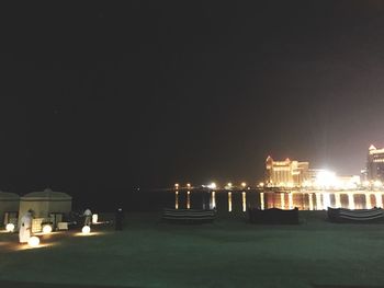 Illuminated buildings by sea against sky at night