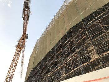 Low angle view of crane at construction site against sky