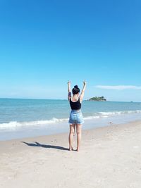 Rear view full length of woman showing peace sign at beach on sunny day