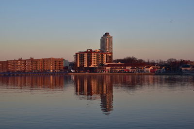 Buildings by river against clear sky at sunset