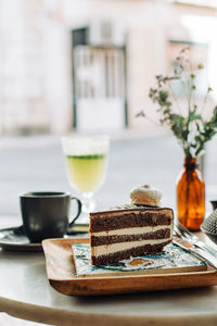 Slice of chocolate cake, flowers, cup of tea on table in outdoors cafe