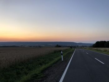 Road amidst field against sky during sunset