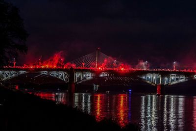 Illuminated bridge over river against sky at night