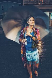 Mid adult woman carrying umbrella while walking on street during monsoon