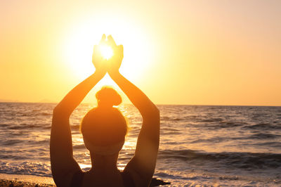 Silhouette woman holding heart shape against sea during sunset