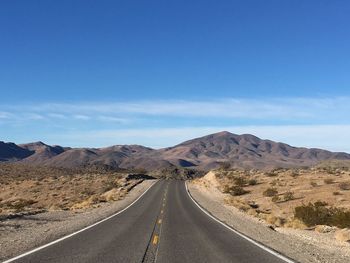 Empty road in desert against blue sky