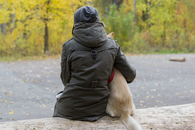 Rear view of woman sitting with dog on retaining wall at park