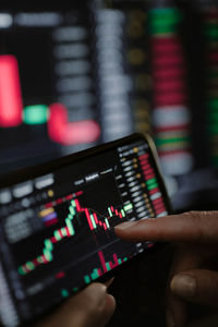 Hand of young business girl looking at trading graphs on office computer and mobile phone