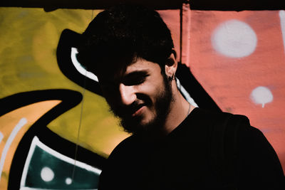 Close-up of smiling man against graffiti wall