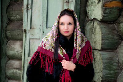 Woman wearing scarf looking away against log cabin