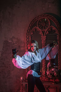 Full length portrait of woman standing against pink wall