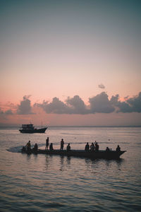 Silhouette people in sea against sky during sunset