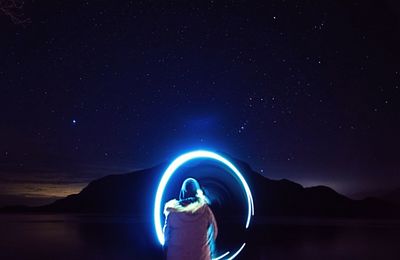 Rear view of person making light painting against sky at night