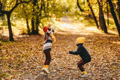 Happy cheerful children in warm clothes have fun walking running in autumn park playing with leaves