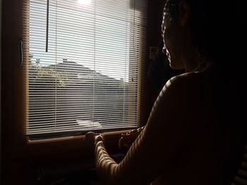 Woman standing by blinds at home