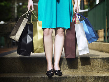Low section of woman holding shopping bags while standing on steps