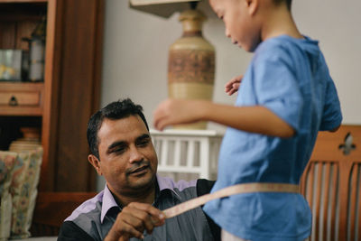 Tailor measuring waist of boy at home