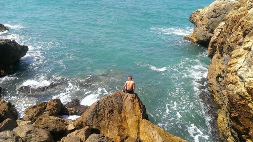 High angle view of shirtless man sitting on rock by sea