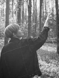 Rear view of man standing by trees in forest