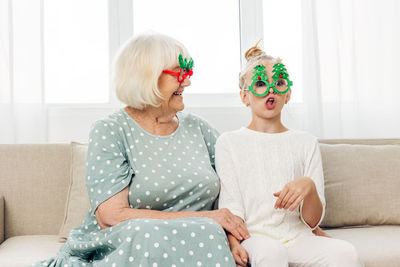 Portrait of smiling mother and daughter sitting on sofa at home